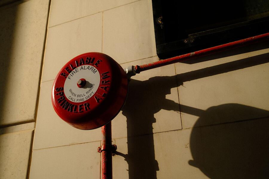A red fire alarm bell mounted on a wall beside its conduit