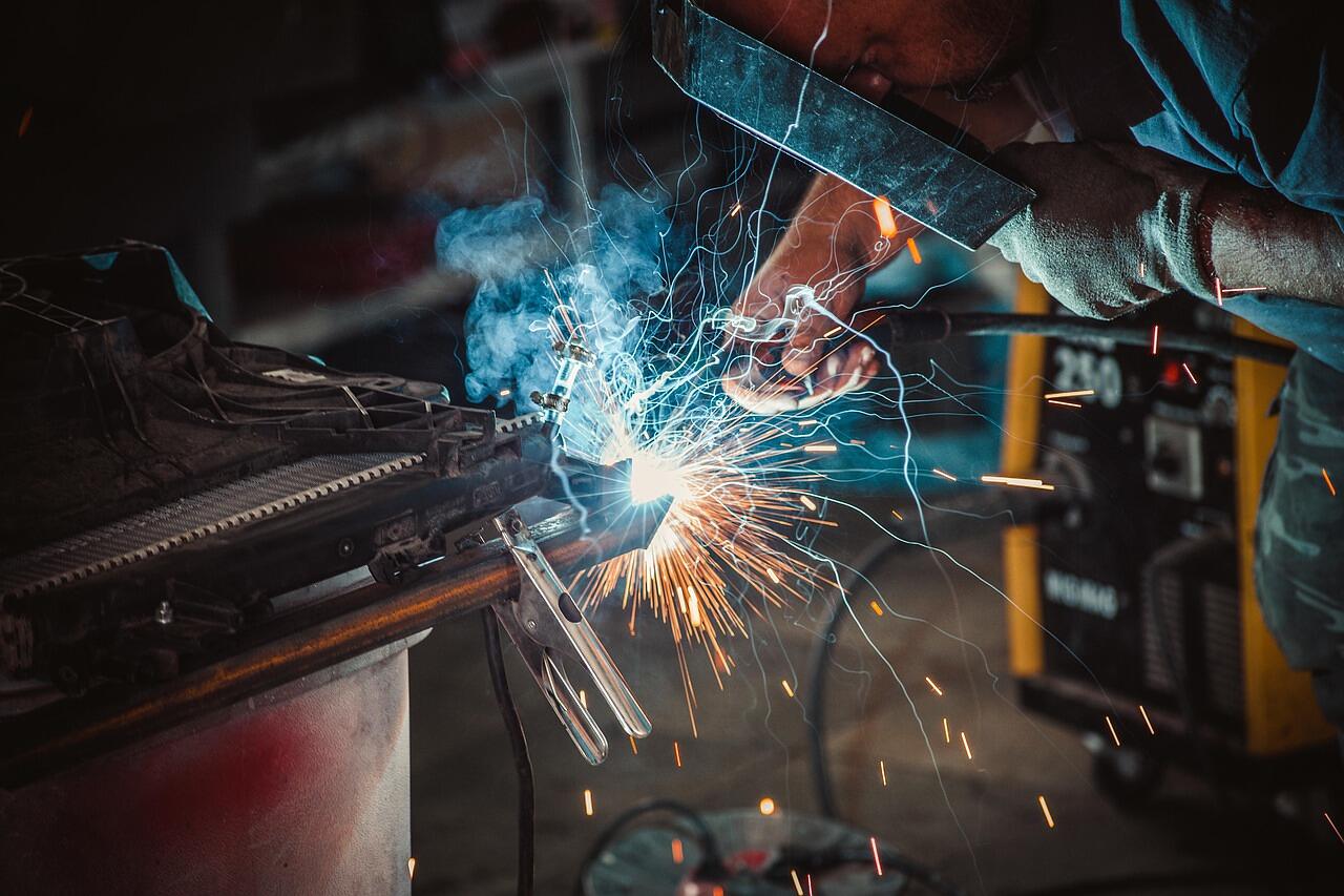 A welder working on steel with sparks falling, face shielded by a helmet